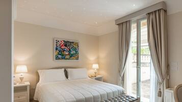 A bedroom with a bed, bedside lamps, a window with curtains, and a wall-mounted artwork.