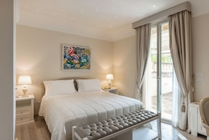 A bedroom with a bed, bedside lamps, a window with curtains, and a wall-mounted artwork.