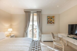 Habitación de hotel con cama, escritorio, silla, televisor y ventana con cortinas.