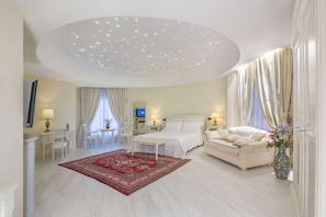A hotel room with a large bed, a sofa, a desk with a chair, a TV, and a ceiling with lights.