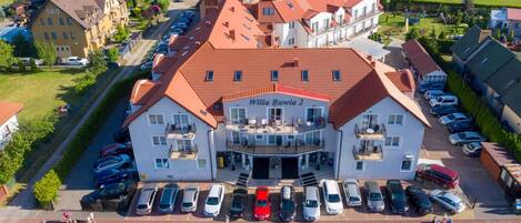 A two-story building with a red-tiled roof, labeled 'Willa Rawia 2,' featuring a central balcony and a parking lot with multiple cars.