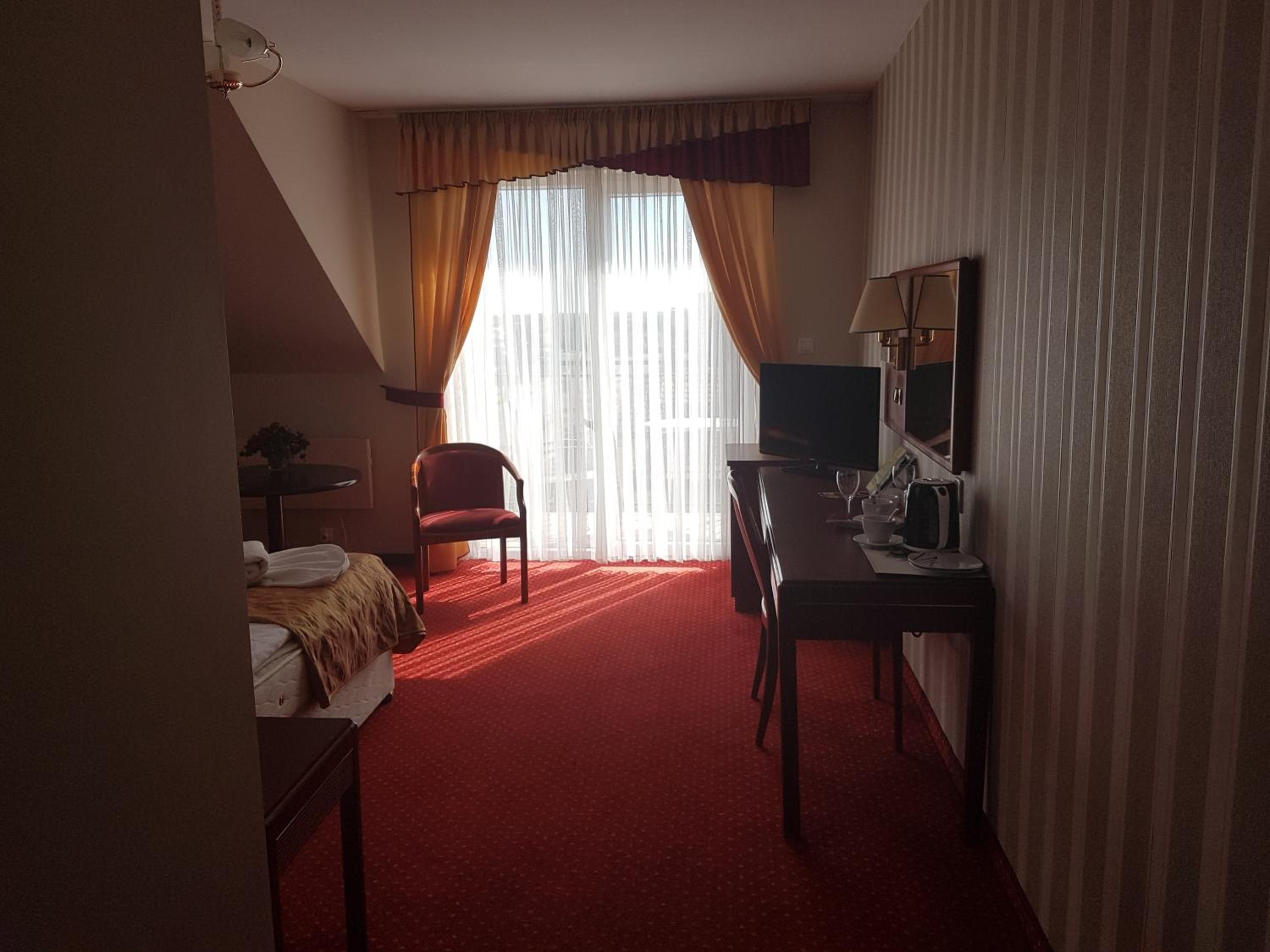 A hotel room with a bed, a desk, a chair, a television, and a window with curtains.
