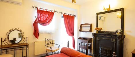 Una habitación con cama, escritorio, sillón, chimenea y espejo.
