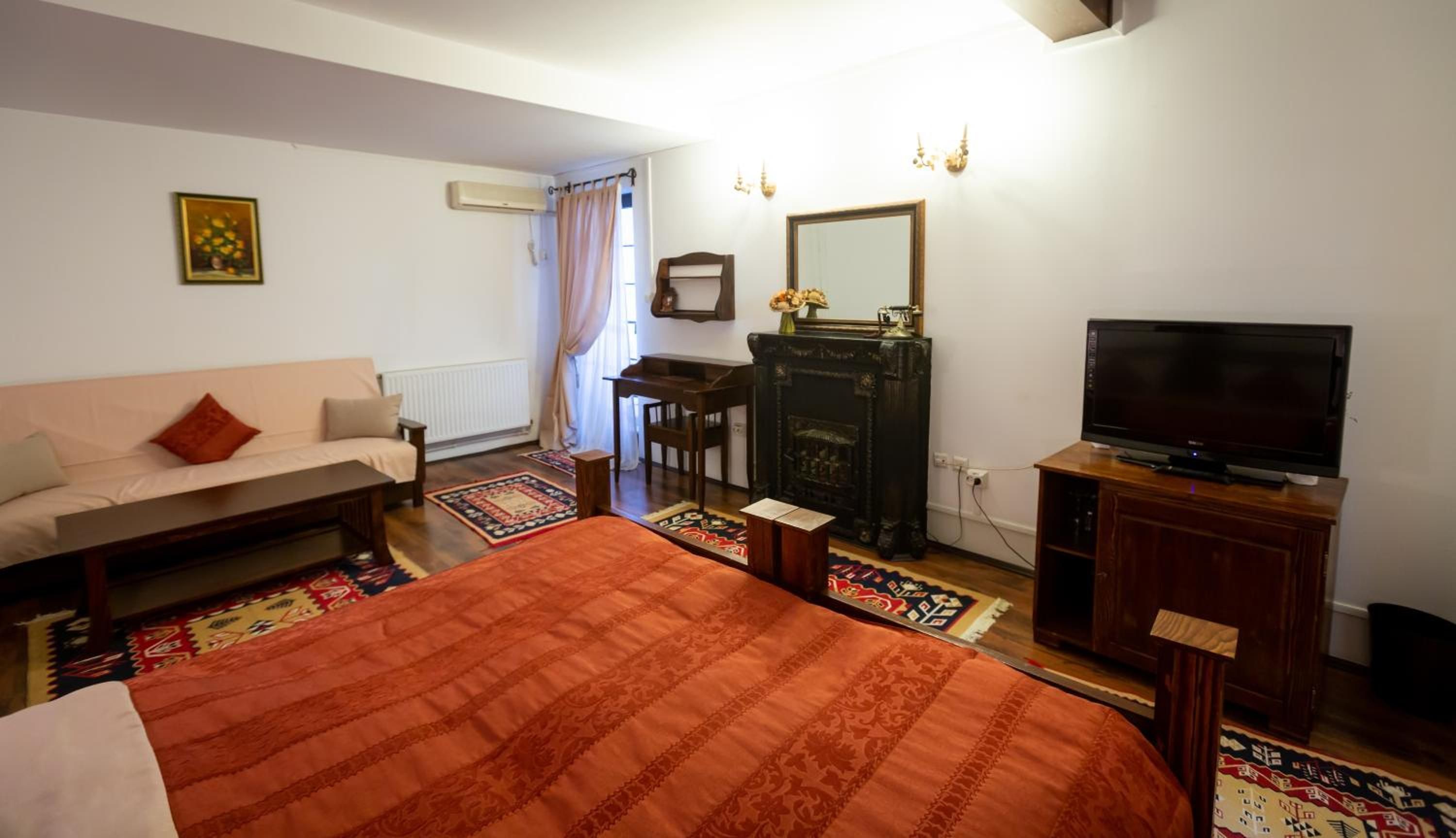 A furnished room with a sofa, a bed, a television, a fireplace, and a mirror.