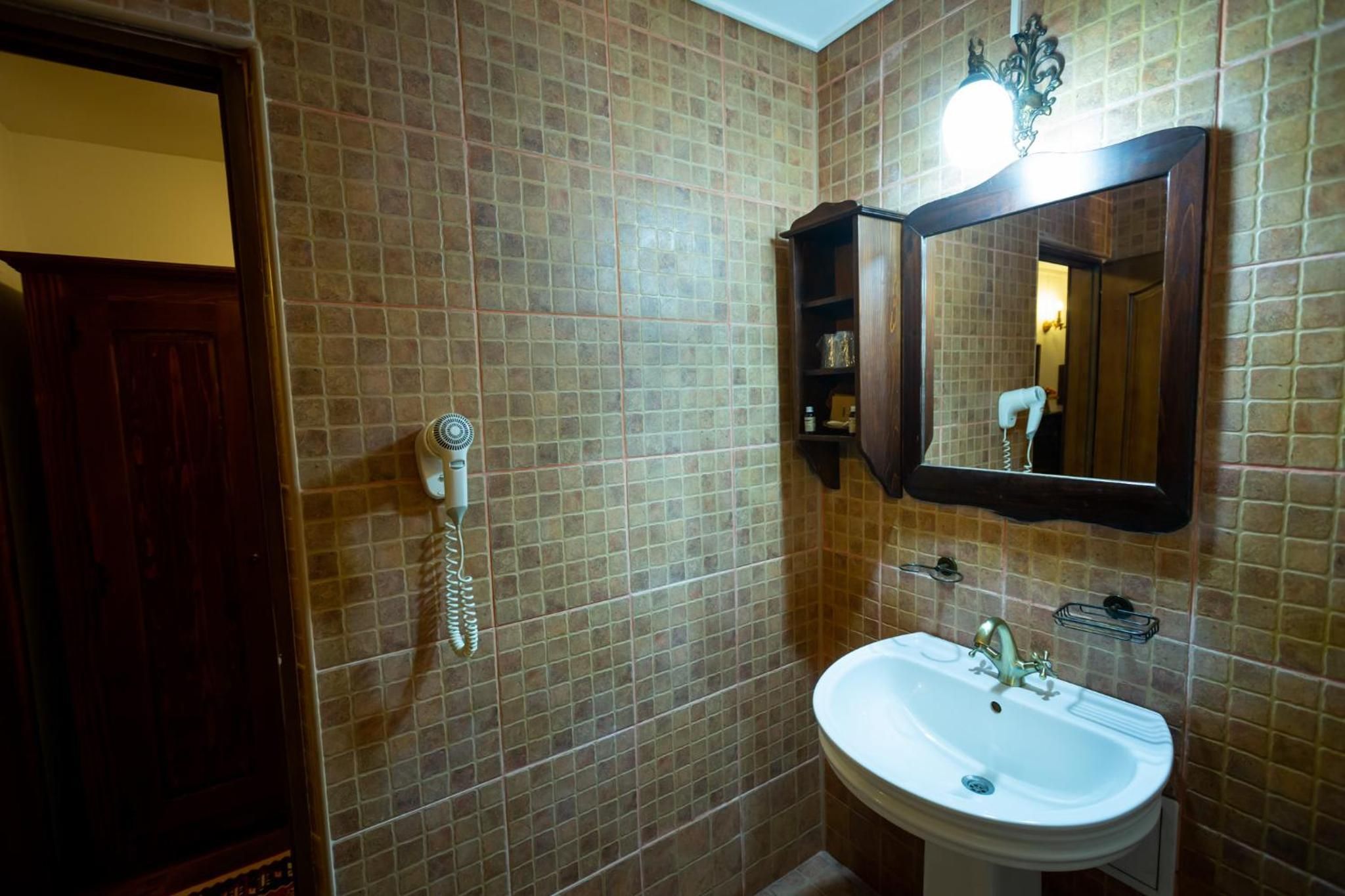 Un baño con pared de azulejos, puerta de madera, lavabo blanco, espejo y secador de pelo.