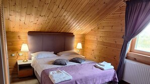 A cozy bedroom with a wooden ceiling, a bed with a purple bedspread, two bedside lamps, and a window with curtains. - Transylvania Mountain Chalet (Bran)