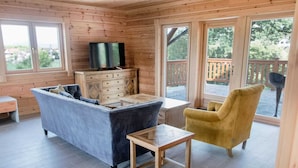 A cozy cabin interior with a sofa, a yellow armchair, a wooden table, and a TV on a dresser. - Transylvania Mountain Chalet (Bran)