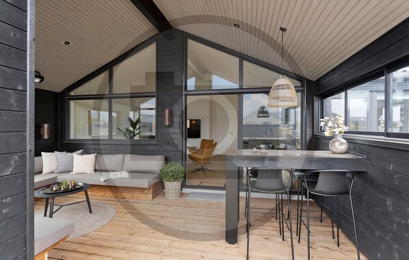 Ein modernes Interieur mit einem großen Glasfenster, einem Essbereich mit Stühlen, einer Couch und einem kleinen Tisch mit Getränken.