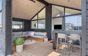 Um interior moderno com piso de madeira, um sofá cinzento, uma pequena mesa redonda e um espaço de bar com duas cadeiras.