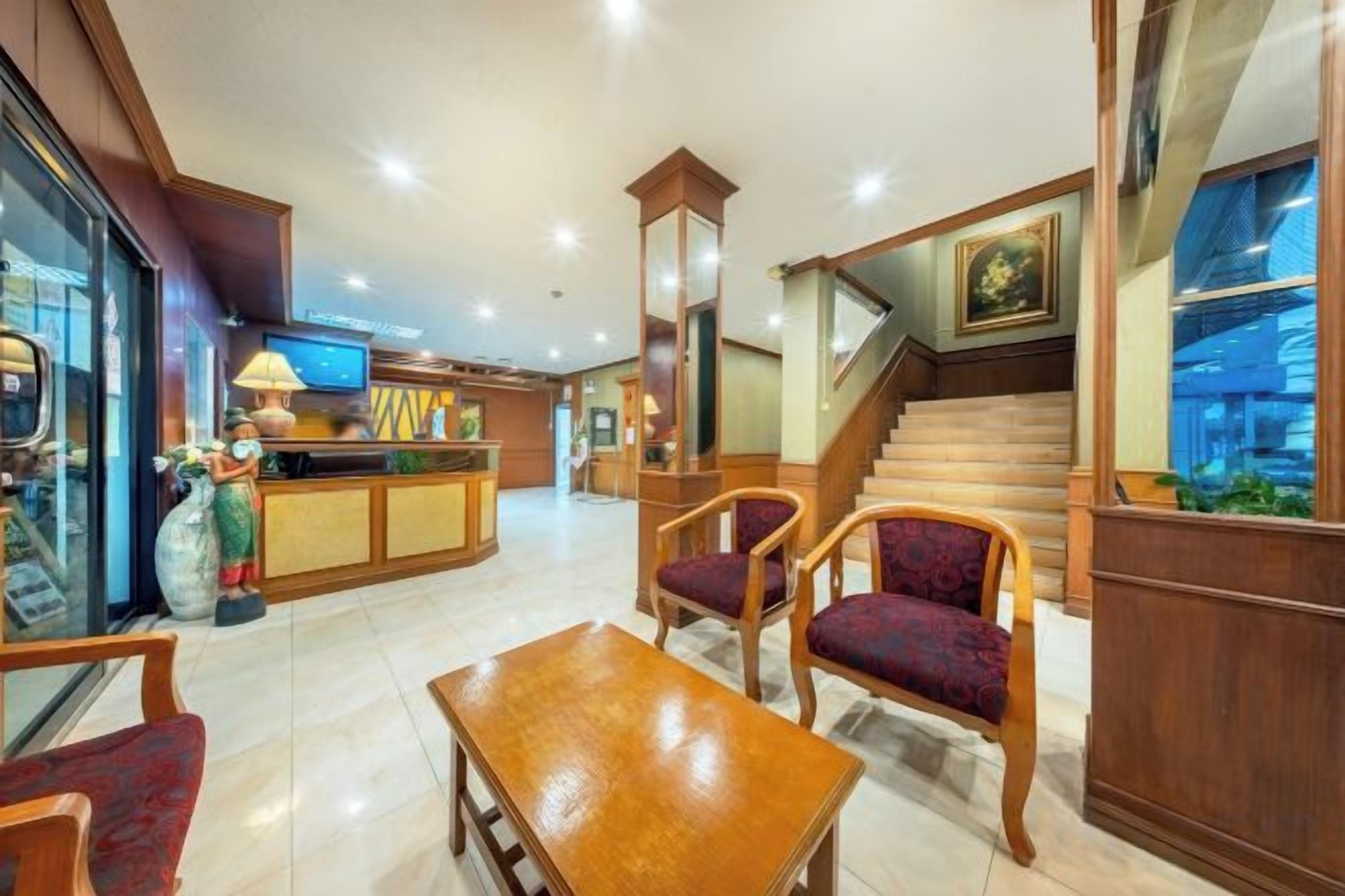 A hotel lobby with a reception desk, seating area, and a staircase.