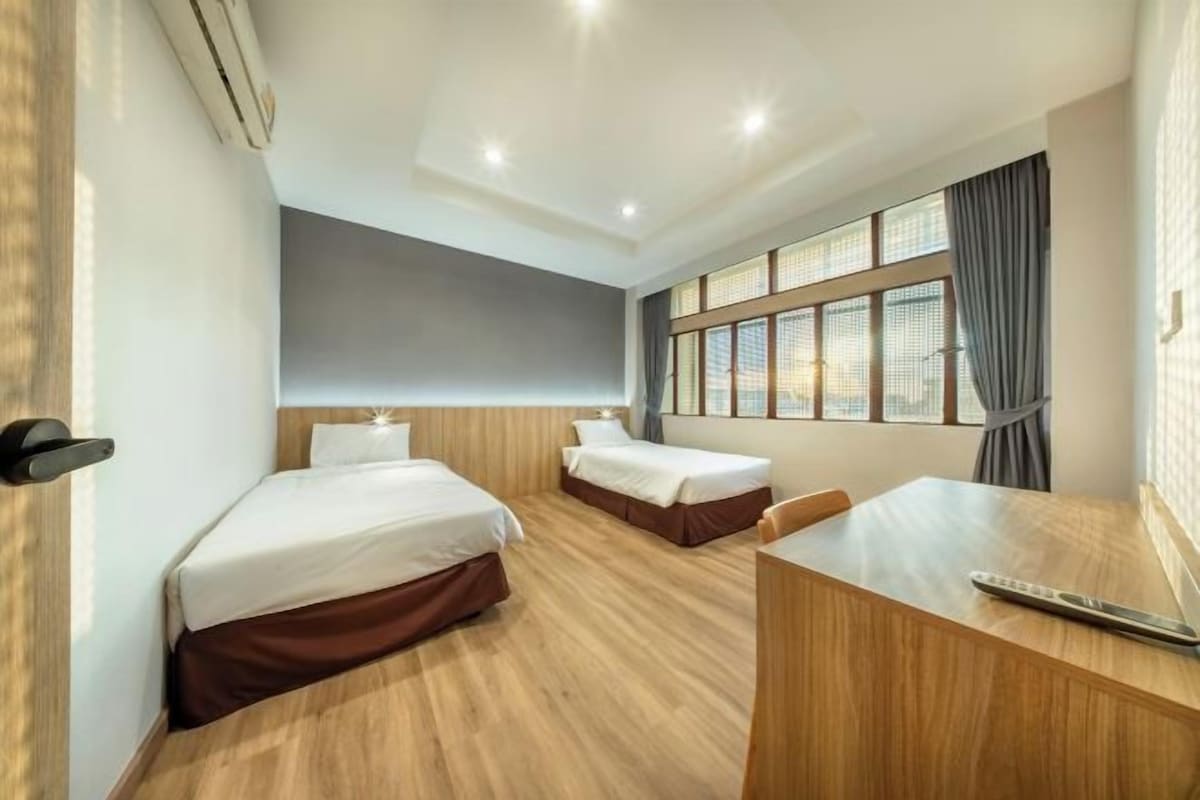 A hotel room with two single beds, a desk, and a large window with curtains.