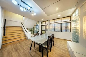 Un interior moderno con una escalera, un comedor con mesa y sillas, y ventanas amplias.
