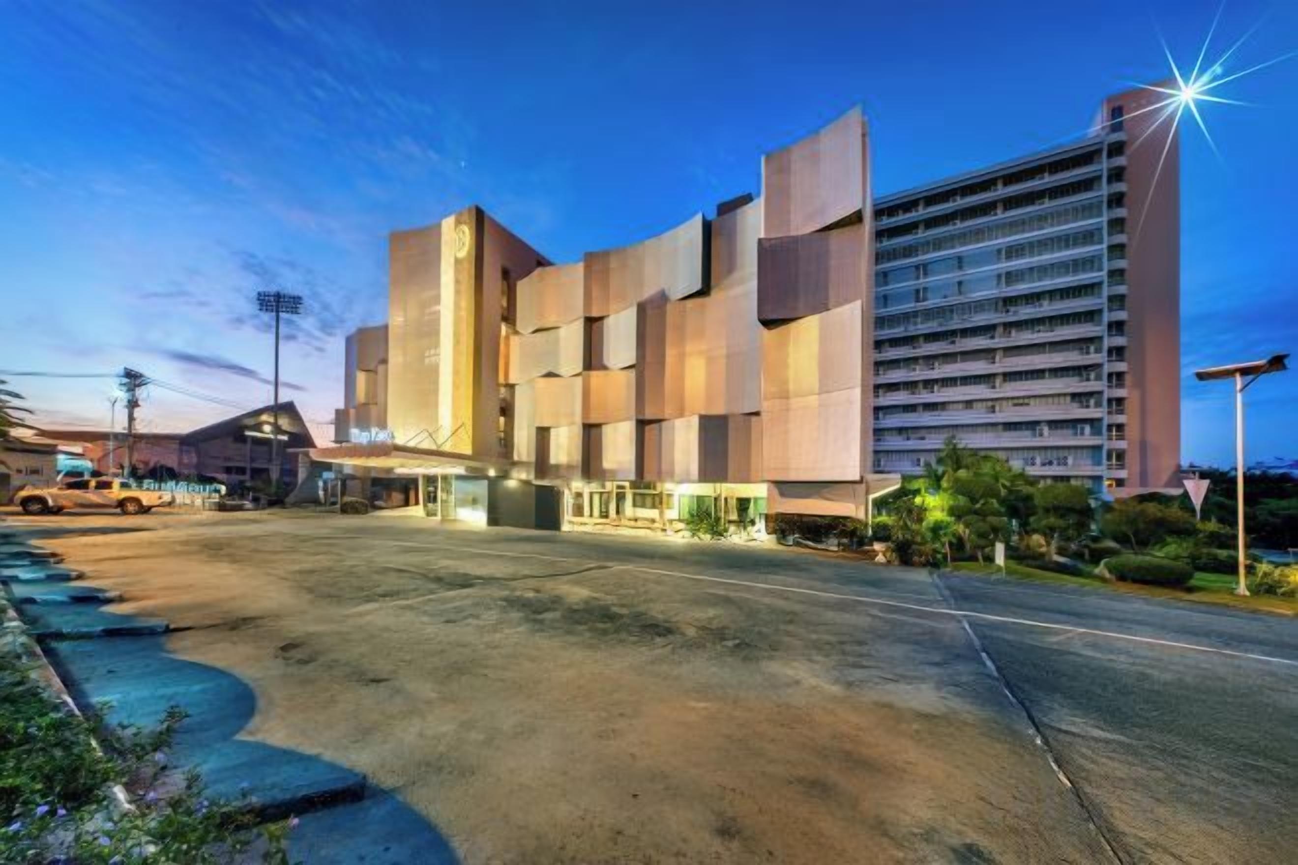 A modern hotel with a unique architectural design, featuring a large parking area and a well-lit entrance.