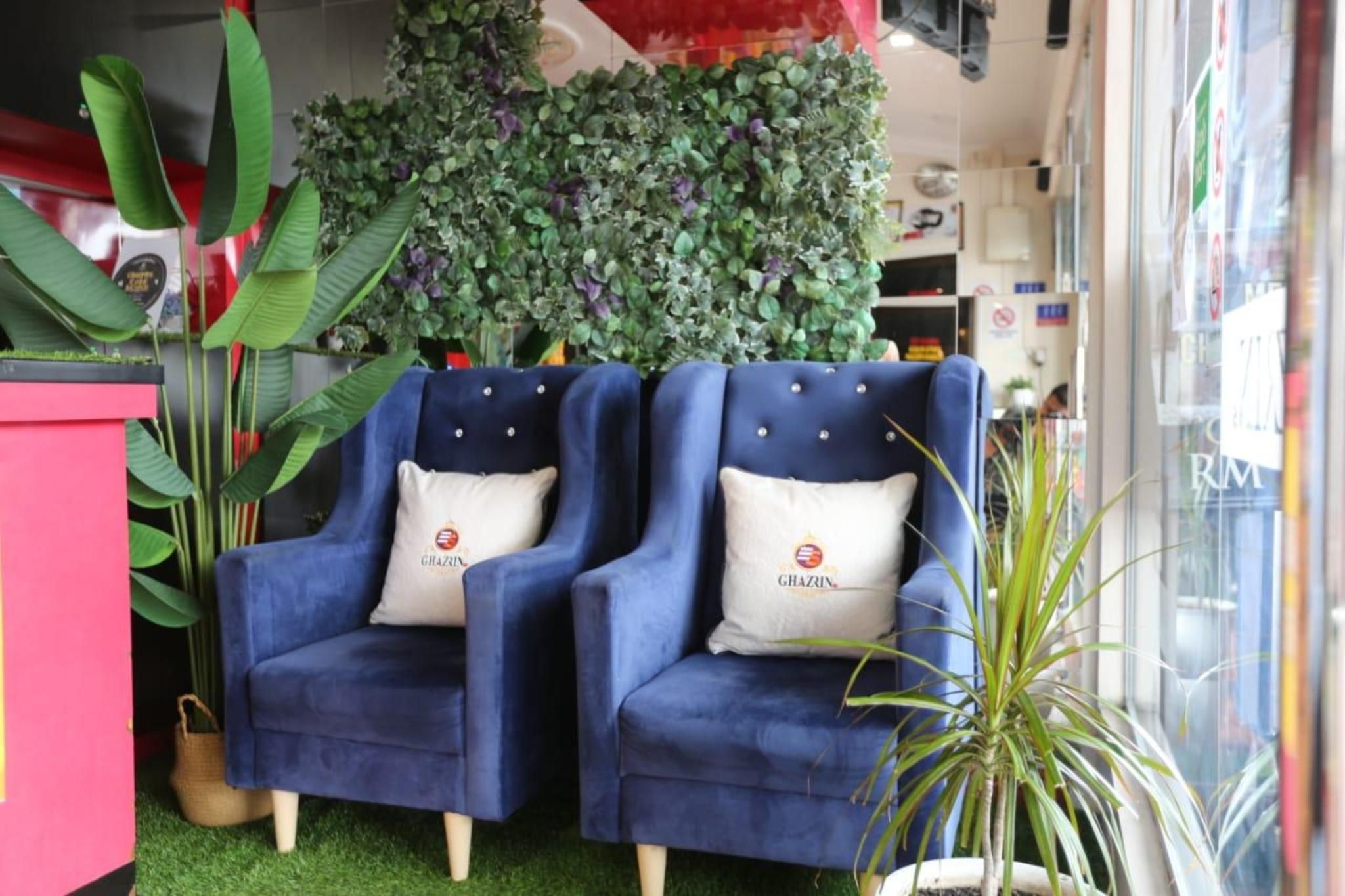 Two blue armchairs with matching cushions, a green artificial grass floor, and a wall of green foliage.