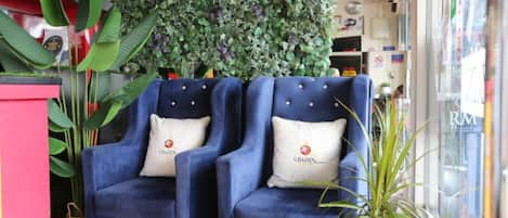 Dos sillones azules con cojines a juego, un suelo de césped artificial verde y una pared cubierta de follaje verde.