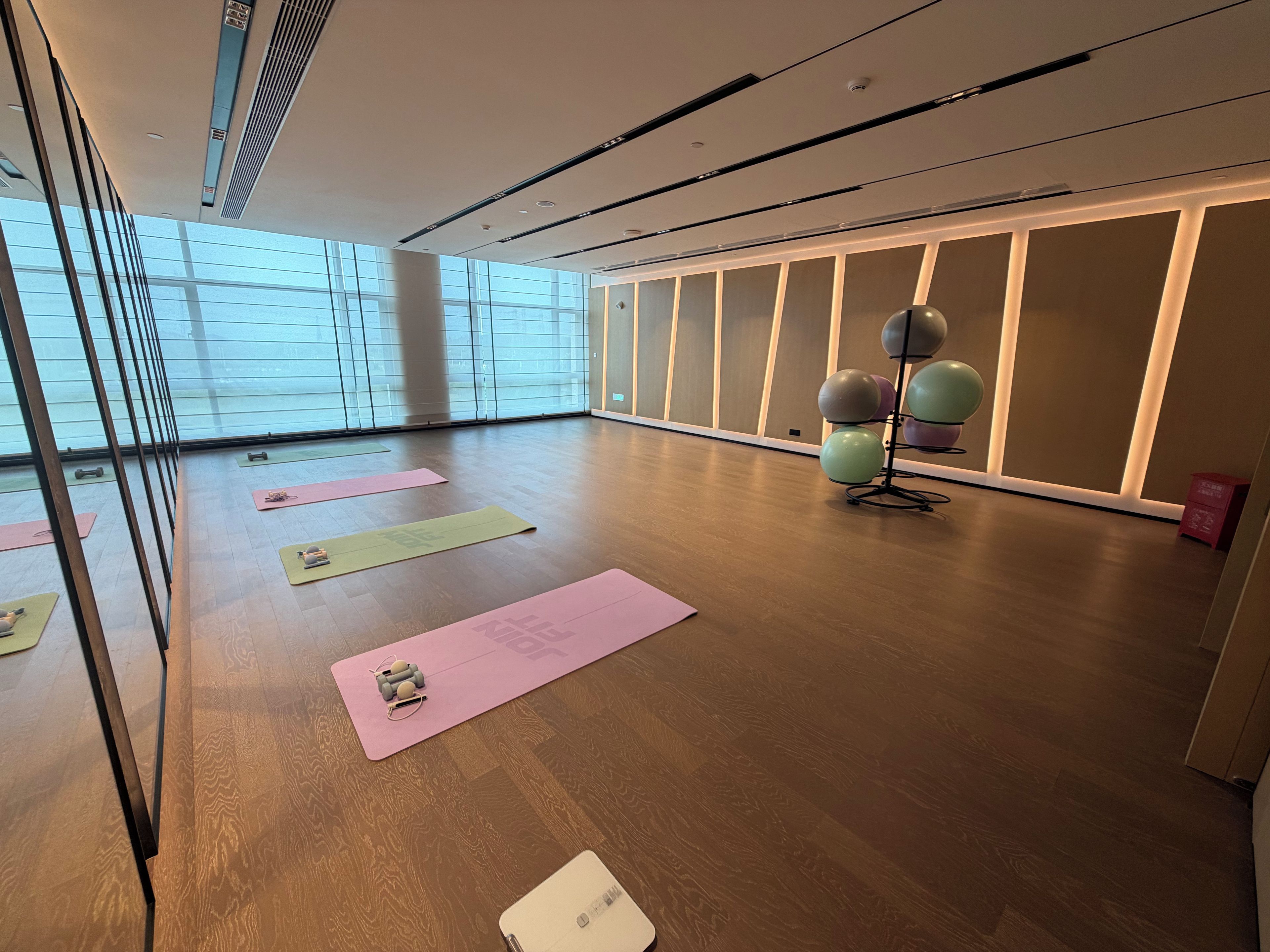 A spacious room with large windows, wooden flooring, and exercise equipment.