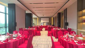 Salão de banquetes com mesas preparadas para refeições, uma tela grande na frente e teto alto com iluminação embutida.