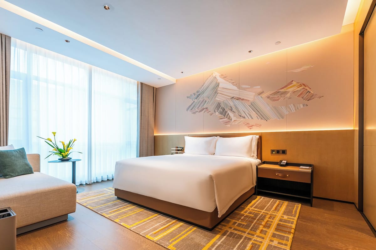 Una habitación de hotel moderna con una cama grande, mesitas de noche, un escritorio y un sofá.