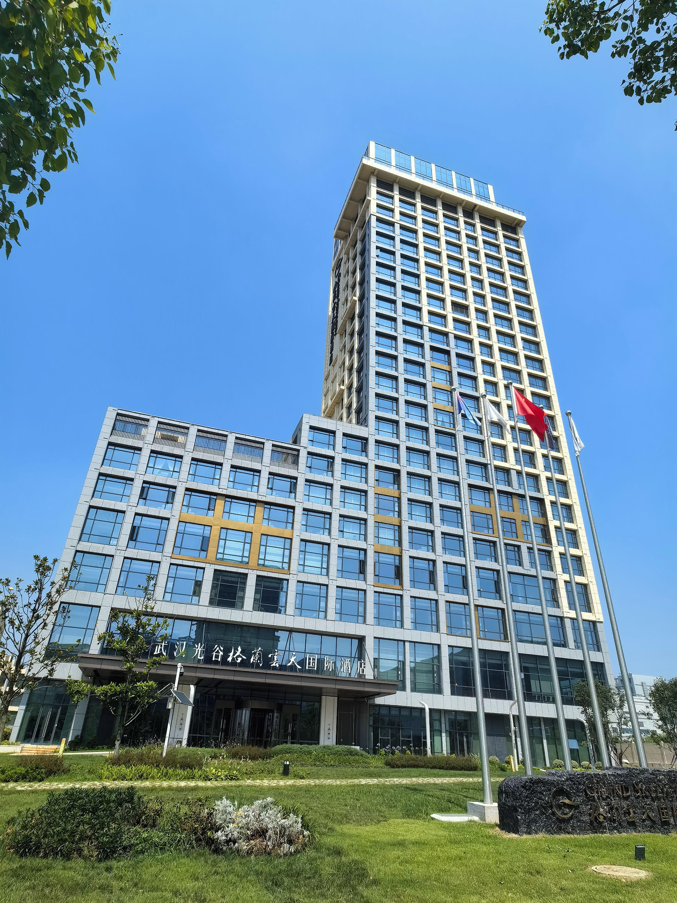 A modern hotel with a prominent flag, large windows, and a well-maintained lawn.