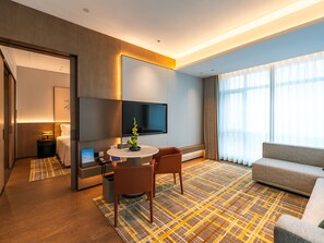 A modern hotel room with a flat-screen TV, a dining area with a table and chairs, a sofa, and a large window with curtains. - Grand Skylight Hotel Wuhan Optics Valley (Wuhan)