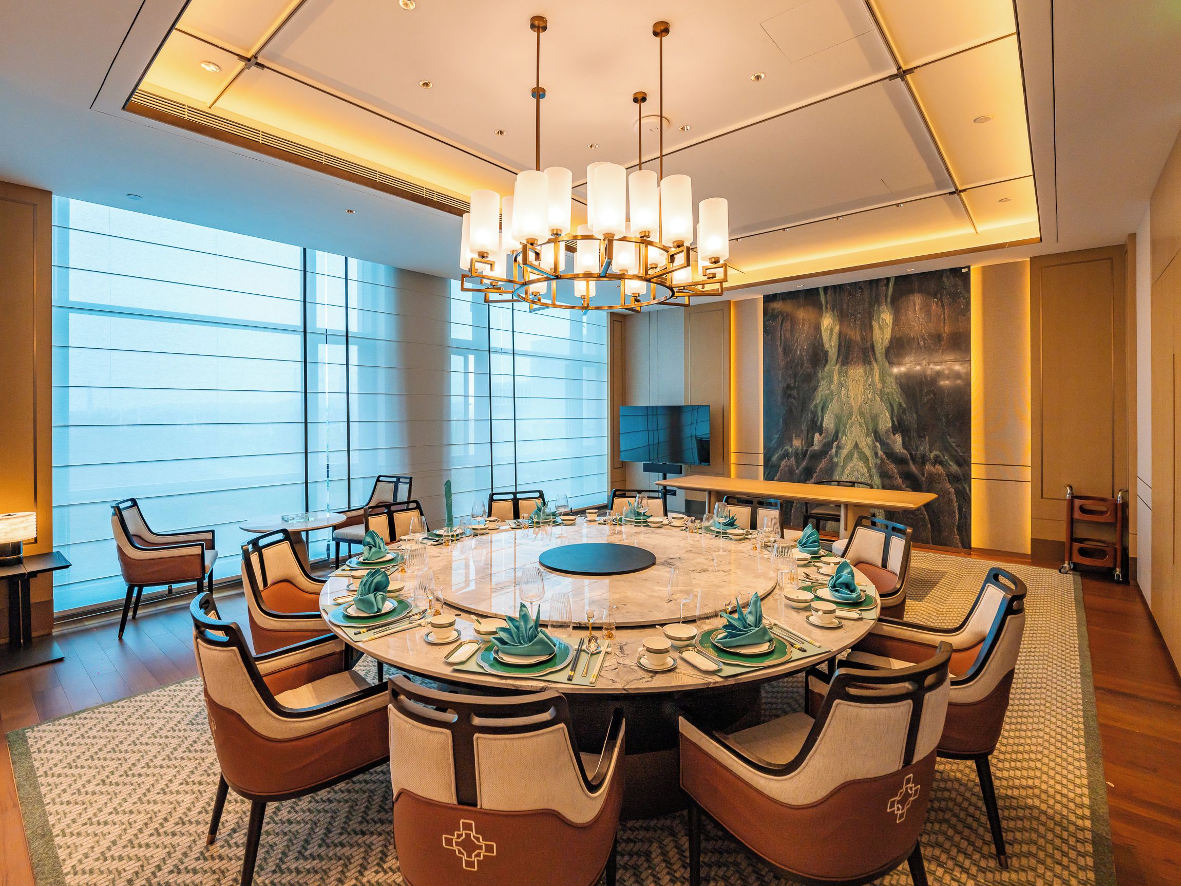 Uma sala de jantar moderna com uma mesa redonda, cadeiras e um candelabro.