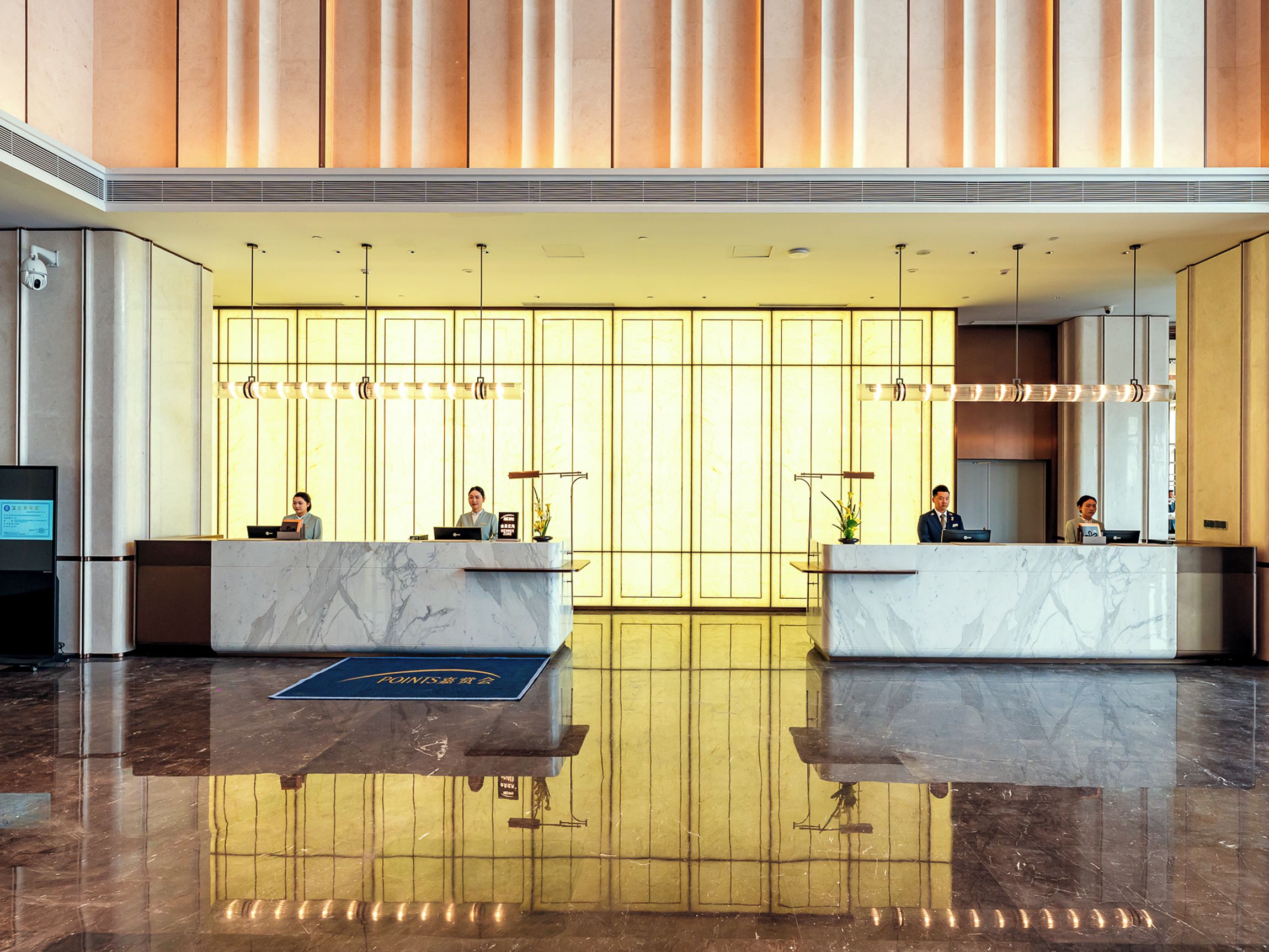Uma área de recepção de hotel com balcões de mármore, um balcão de atendimento e uma parede grande com painéis verticais.