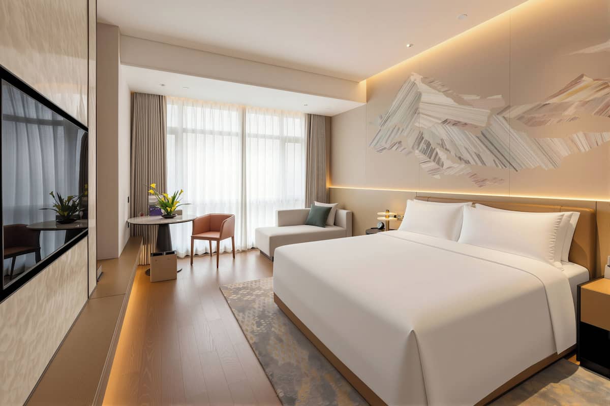 Una habitación de hotel moderna con una cama grande, un escritorio, una silla y un televisor.