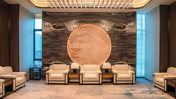 A lobby with a large circular wall art, a modern chandelier, and a seating area with chairs and tables.