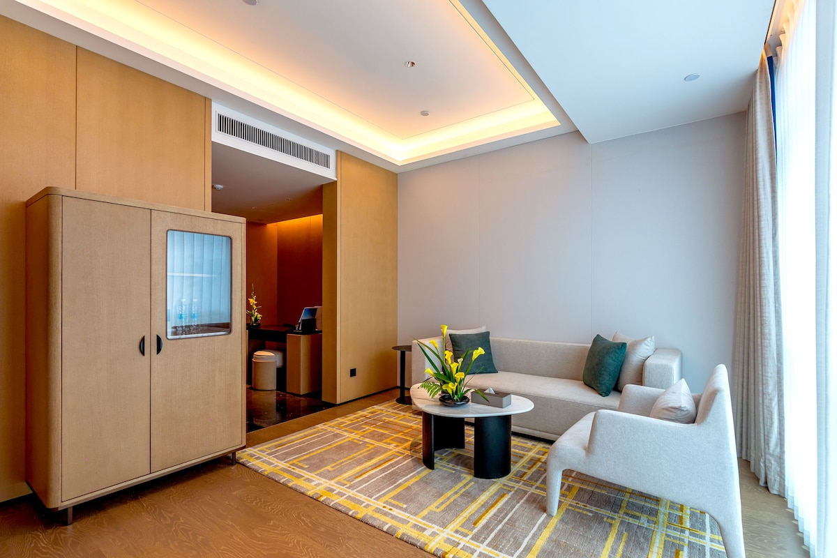 A modern hotel room with a sofa, a coffee table, a cabinet, and a view of the bathroom.