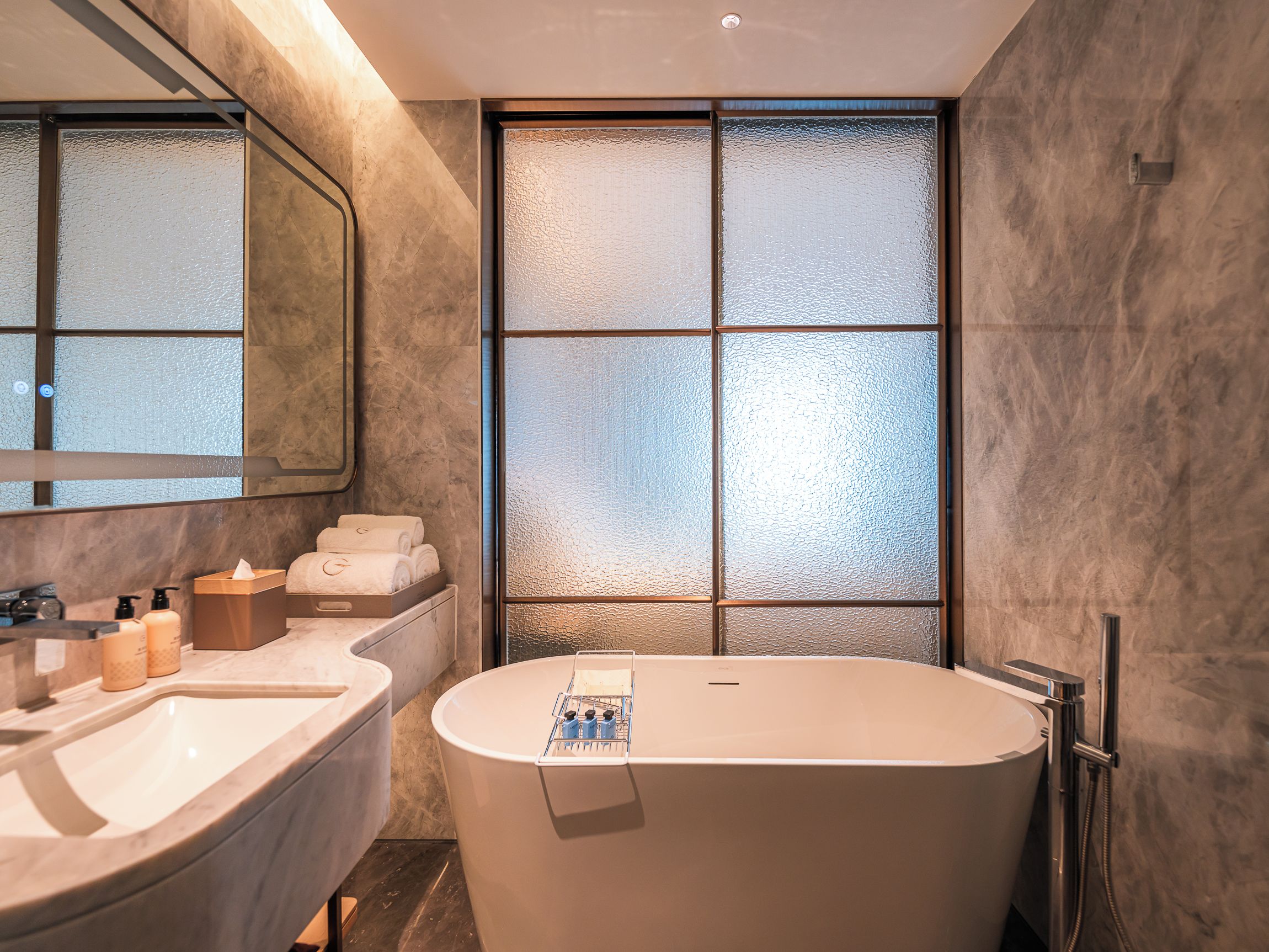 Une salle de bain moderne avec une baignoire sur pieds, un grand miroir et une fenêtre en verre dépoli.
