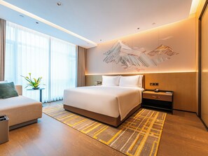 Una habitación de hotel moderna con una cama grande, mesitas de noche, un escritorio y un sofá.
