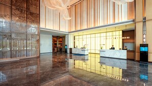 A spacious lobby with a reflective marble floor, a reception desk, and a decorative wall with intricate patterns. - Grand Skylight Hotel Wuhan Optics Valley (Wuhan)