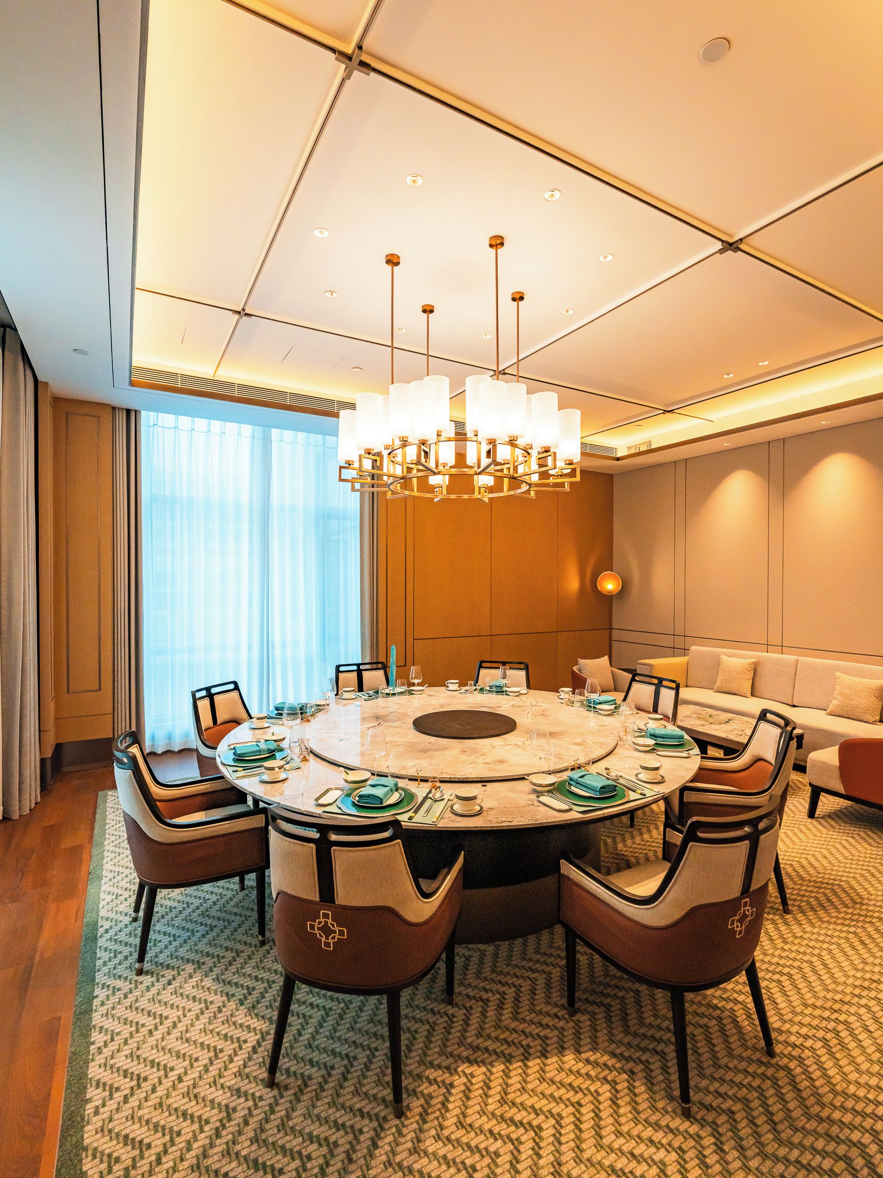 A conference room with a round table, chairs, a chandelier, and a sofa.