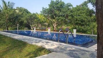 A swimming pool with lounge chairs and a tree-lined background.