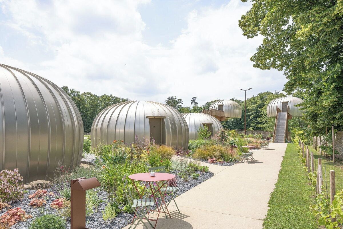 A pathway leading to spherical structures with doors, surrounded by a garden with various plants and a small table with chairs.