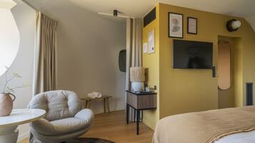A hotel room with a bed, a round table, a chair, a small table with a vase, and a wall-mounted TV.