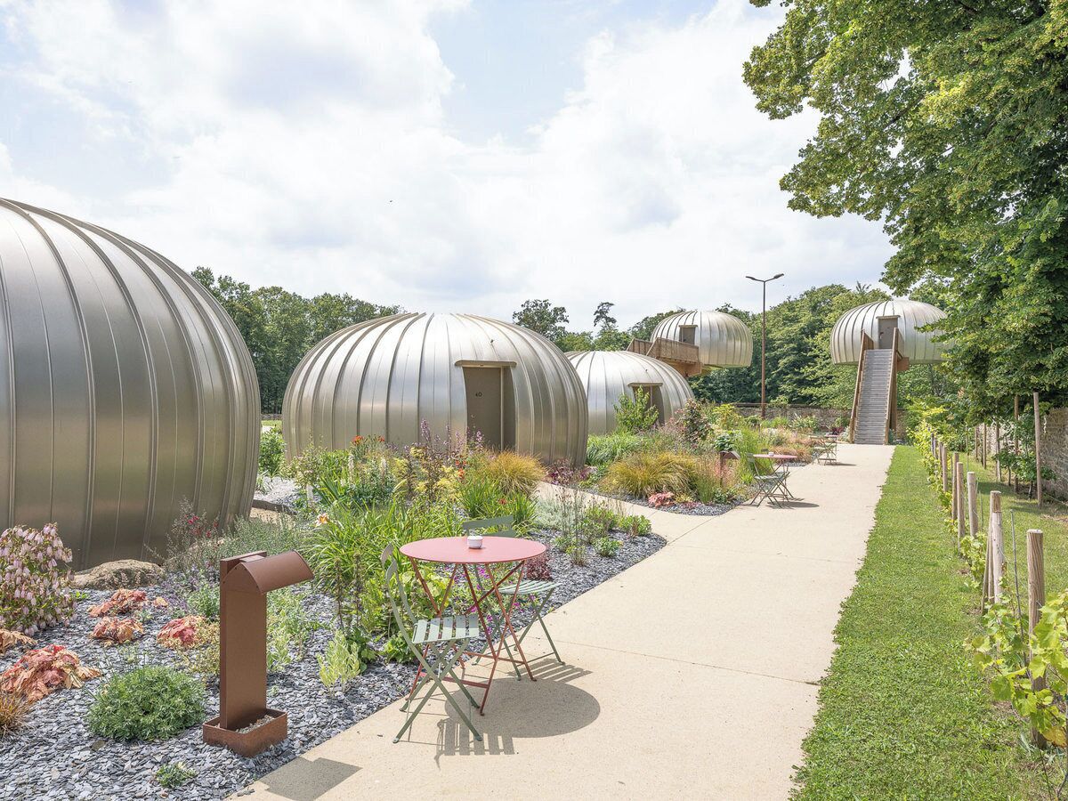A pathway leading to spherical structures with doors, surrounded by a garden with various plants and a small table with chairs.