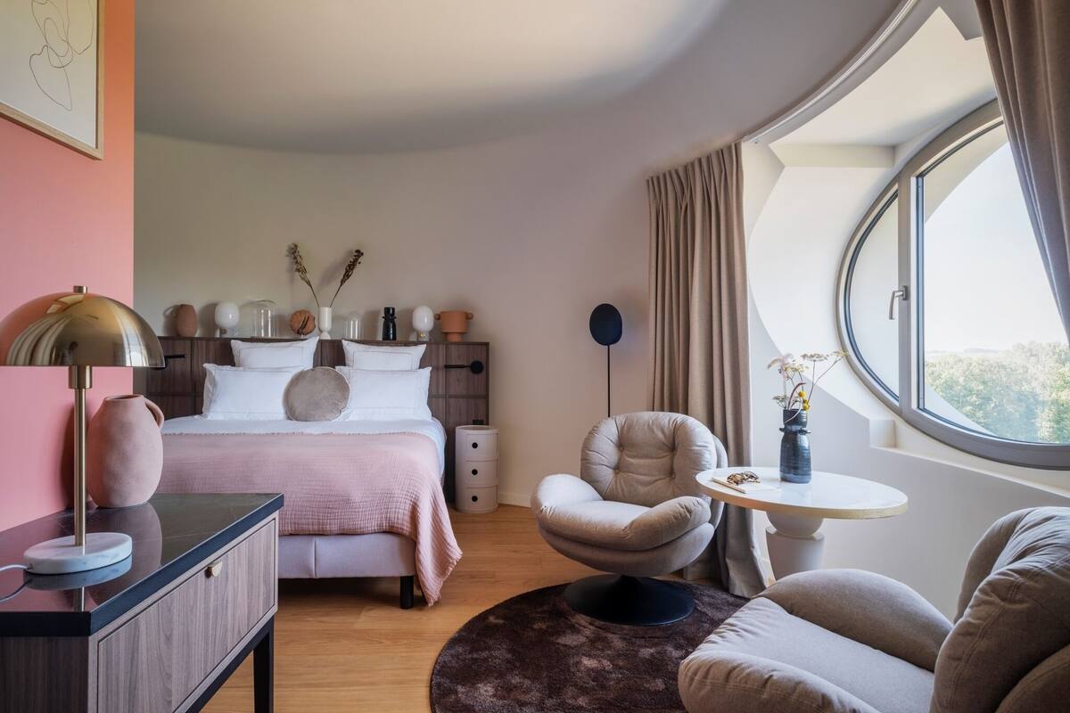 Un dormitorio con cama, mesita de noche, silla y ventana con cortinas.