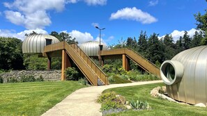 A modern architectural structure with a central staircase leading to a dome-like building, surrounded by greenery and a clear sky. - Hotel-spa L'essenciel - Château Des Pères (Piré-Chancé)