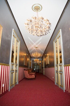 A hallway with a red carpet, chandeliers, and gold-framed doors. - Nf Palace Old City Bucharest (Bucharest)