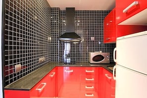Una cocina con paredes de azulejos negros, encimera roja y campana extractora de acero inoxidable.