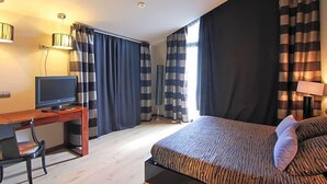 A hotel room with a bed, a desk with a television, and curtains. - Dolcet L Hotel (Alàs i Cerc)