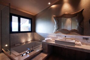 A modern bathroom with a large bathtub, a vanity with a mirror, and a view of the outdoors through a window. - Dolcet L Hotel (Alàs i Cerc)
