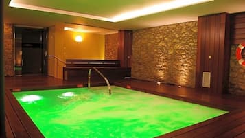 A spa area with a heated pool, wooden flooring, stone wall, and a bench.