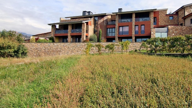 A modern multi-story building with balconies, stone walls, and a grassy foreground. - Dolcet L Hotel (Alàs i Cerc)