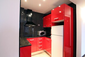 A modern kitchen with red cabinets, a black backsplash, and a white refrigerator. - Dolcet L Hotel (Alàs i Cerc)