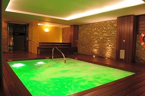 Un área de spa con piscina climatizada, suelo de madera, pared de piedra y un banco.