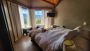 Un dormitorio con una cama, un banco, un televisor y una ventana con cortinas.