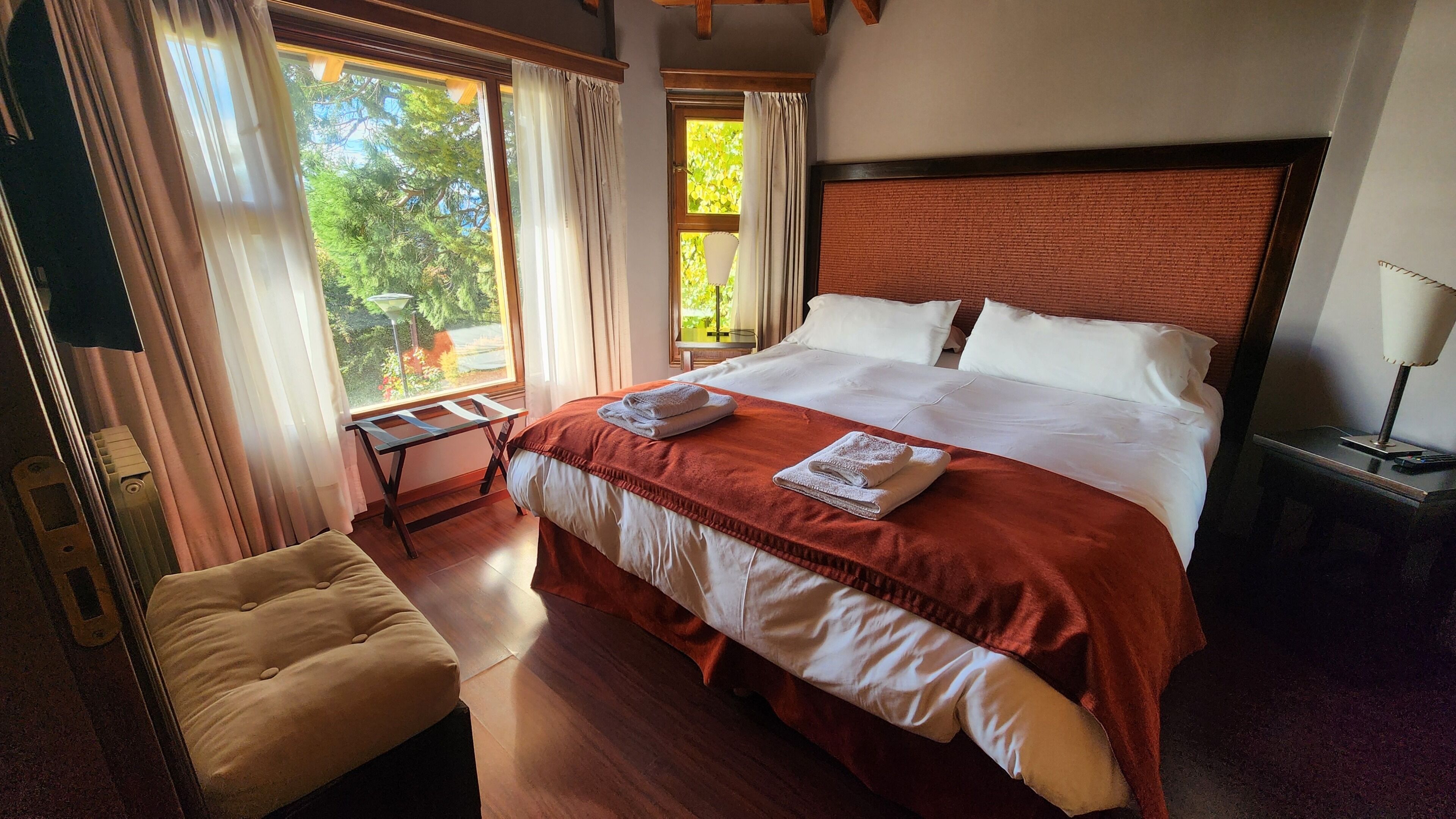 Una habitación de hotel bien iluminada, con una cama grande, una mesita y un banco.