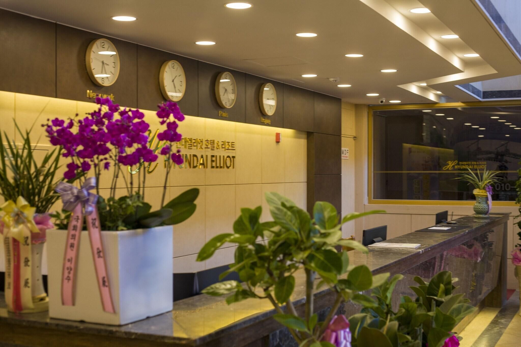 A reception area with a reception desk, multiple clocks, and potted plants.